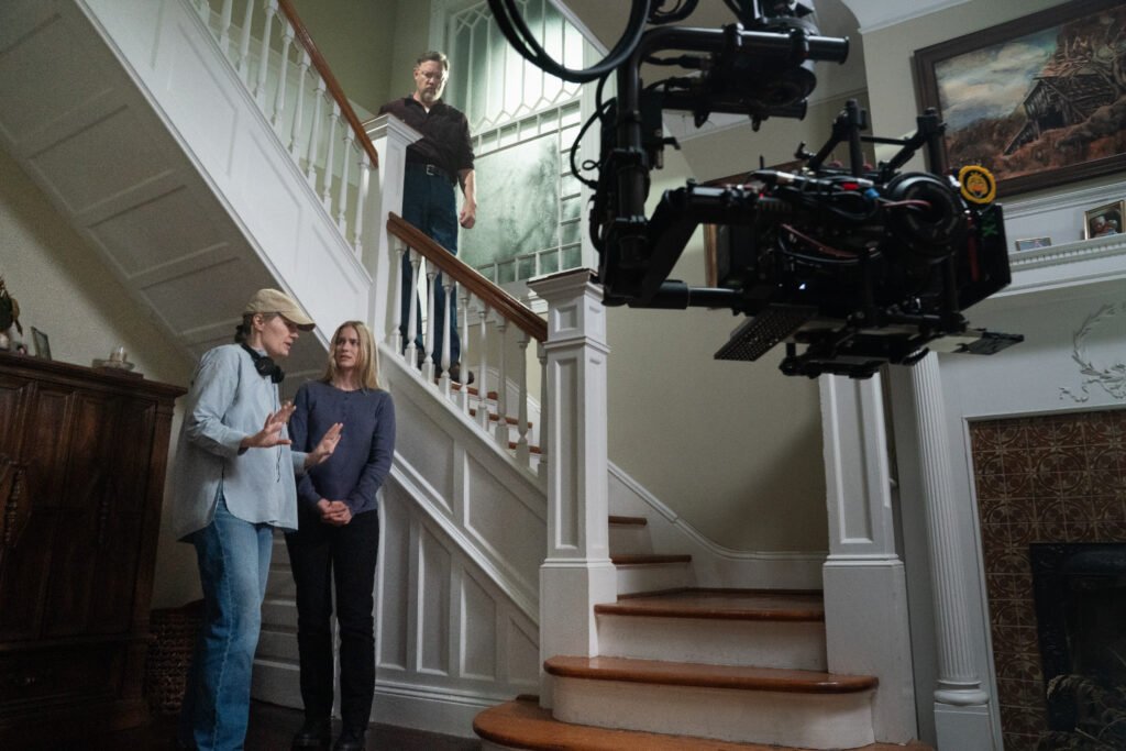 alt="Behind‑the‑scenes photo from 'Five Nights at Freddy’s 2' showing Josh Hutcherson sitting at a cluttered control‑room desk while director Emma Tammi stands beside him giving notes, with blue‑tiled walls, a fan, and a bulletin board in the dimly lit set."
