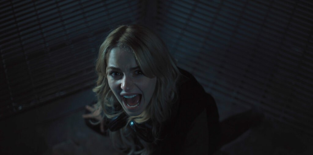 alt="Scene from 'Five Nights at Freddy’s 2' showing a terrified young woman screaming in a dim, metallic room, lit by harsh shadows that heighten the film’s tense, horror‑driven atmosphere."
