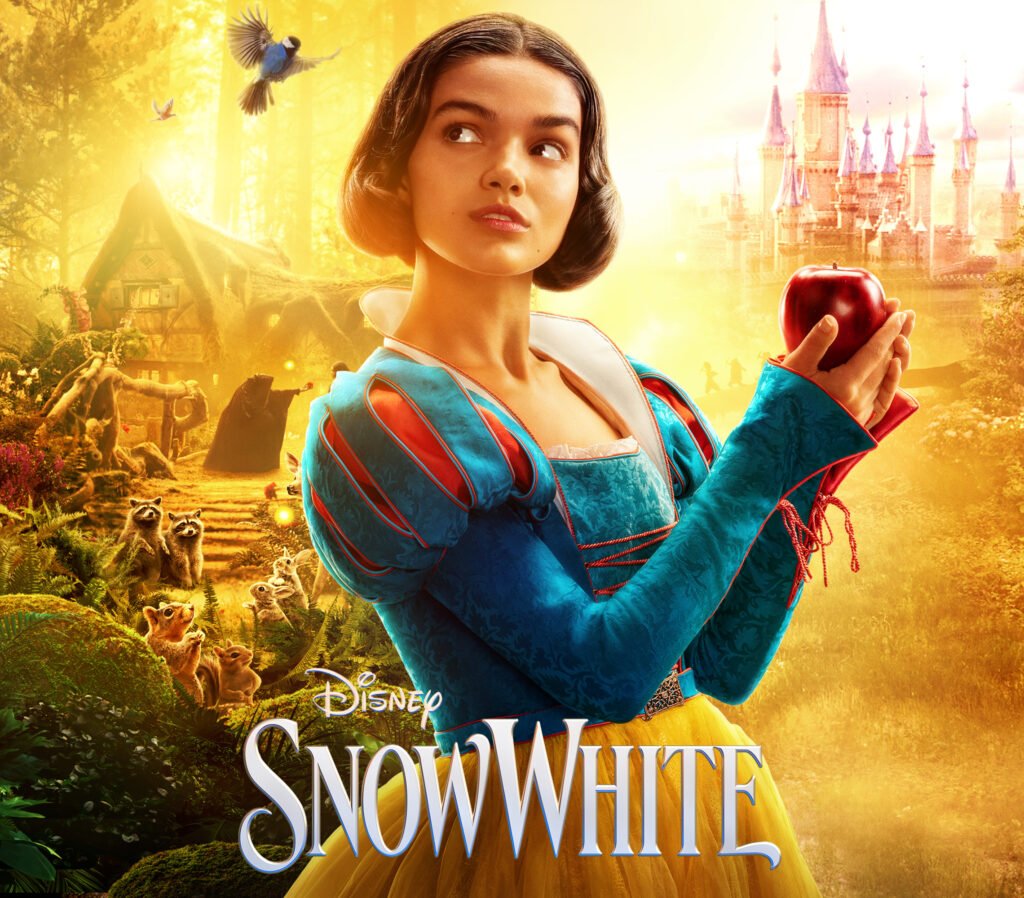 alt="Disney's 2025 Snow White poster featuring Snow White holding a red apple in a golden forest with a cottage, castle, and forest animals in the background."
