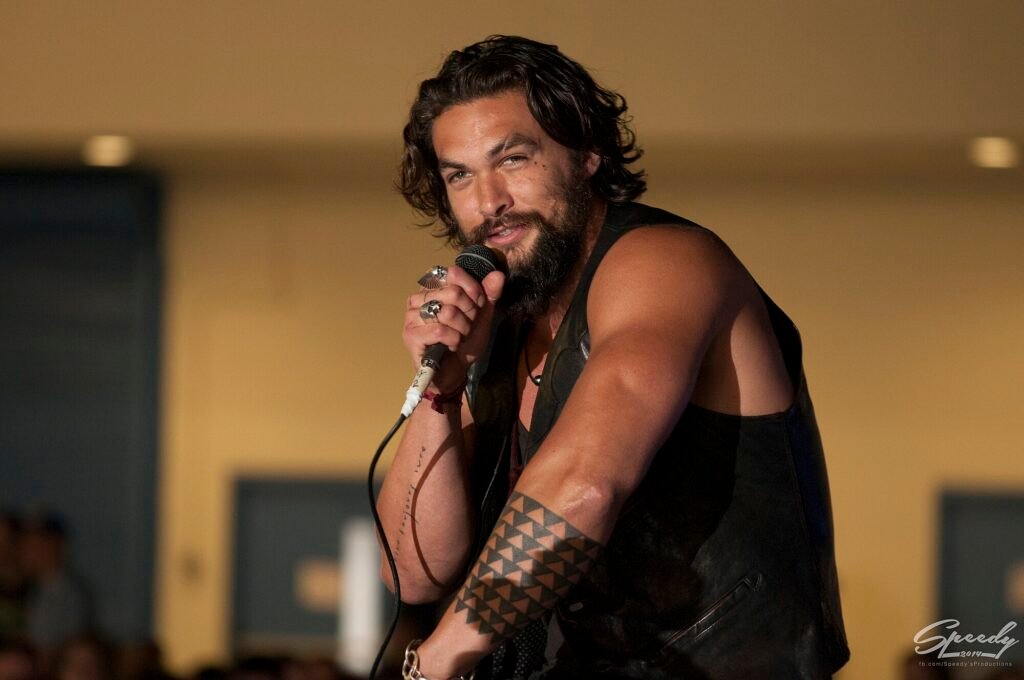 Alt="Jason Momoa speaking to fans while wearing a black leather vest."
