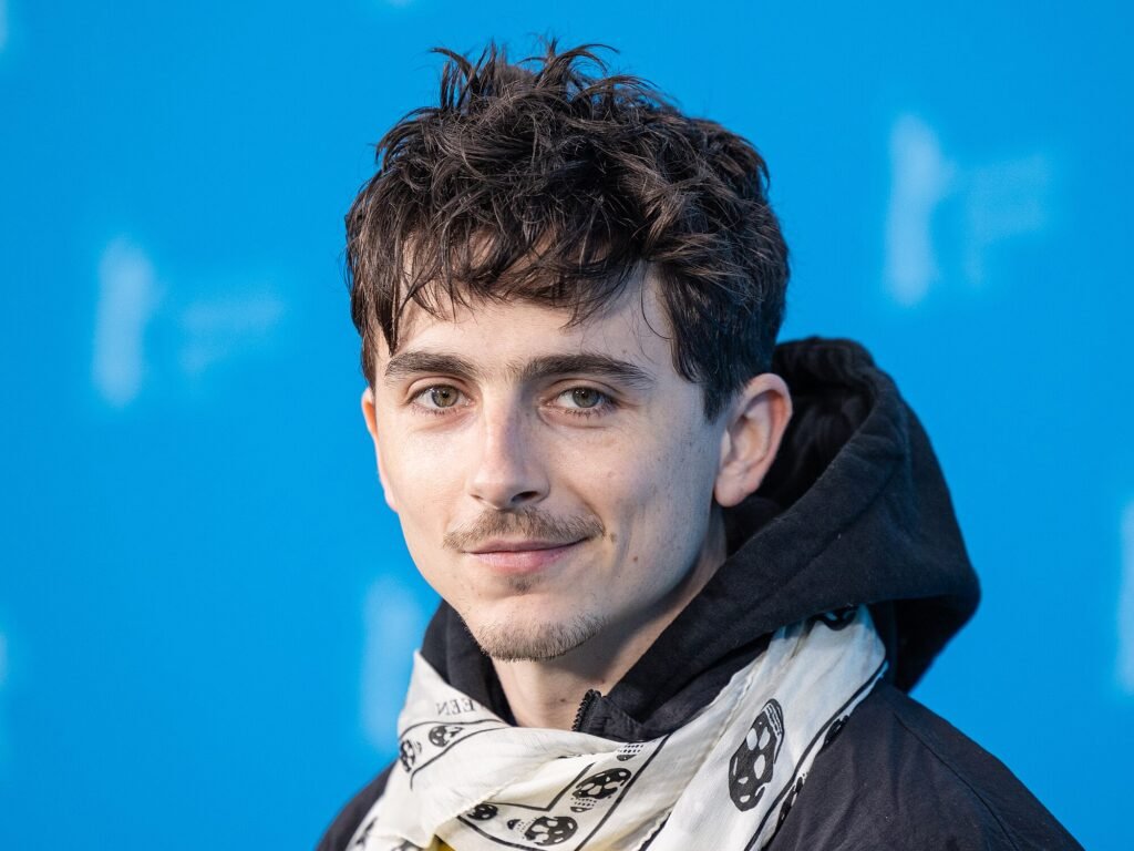 Alt="Timothée Chalamet posing at a film event in a black hoodie and skull-patterned scarf, as anticipation builds for the first Dune Part Three teaser trailer."