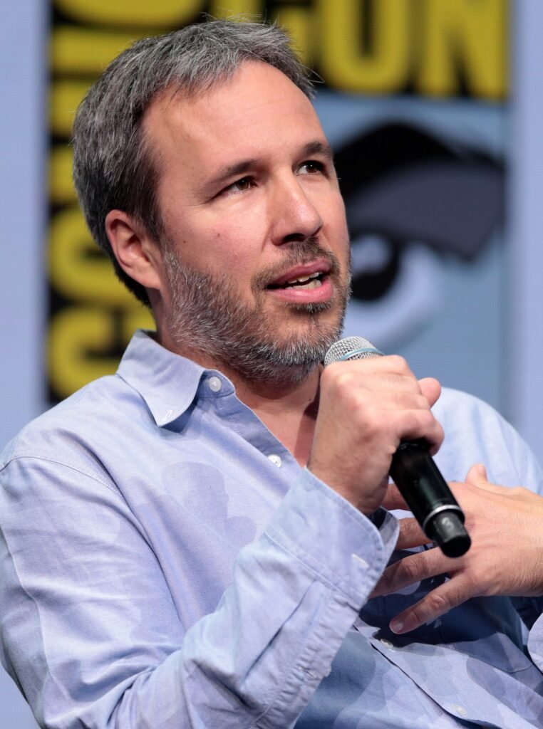 Alt="Denis Villeneuve speaking onstage at San Diego Comic-Con, discussing the future of the Dune saga. The first teaser trailer for Dune Part Three."