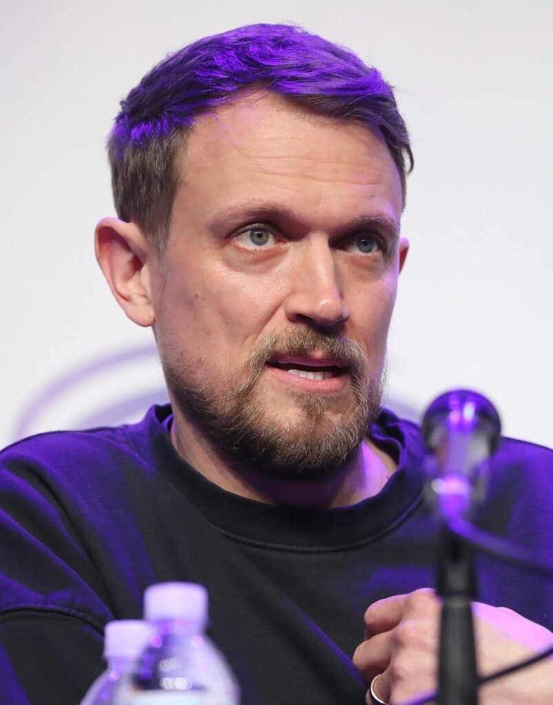 Alt = Matt Bettinelli-Olpin speaking at the 2024 WonderCon in Anaheim, California. Ready or not 2