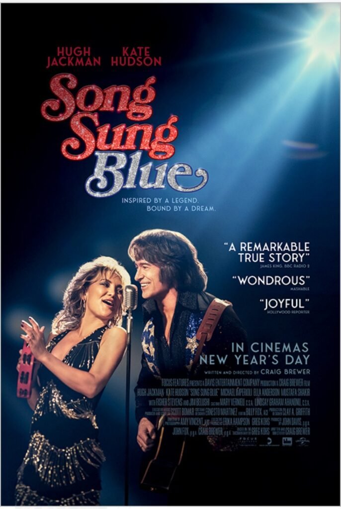 alt="Poster for the film 'Song Sung Blue' showing a man and woman performing together on stage in glittery outfits, sharing a microphone as he plays guitar and she holds a tambourine, with bright spotlighting, glitter‑text title, glowing reviews, and a New Year’s Day cinema release note."
