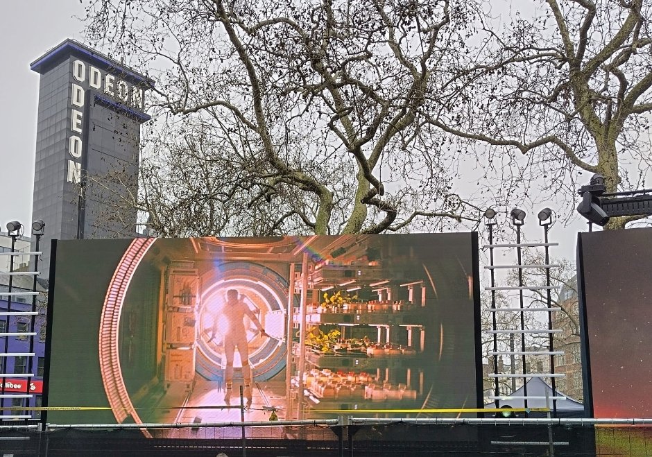 Alt text:  
Outdoor setup for the Project Hail Mary London premiere, showing a large screen displaying a sci‑fi corridor scene with the Odeon cinema in the background.