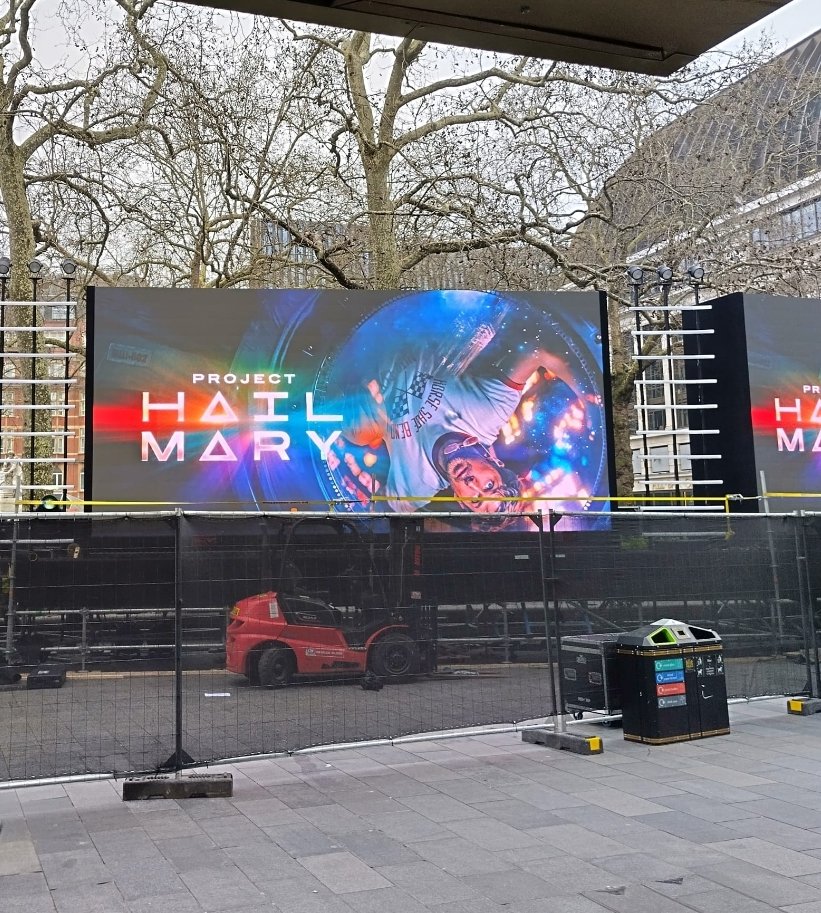 Alt text:  
Large digital billboard for “Project Hail Mary” being set up in London, with construction equipment, fencing, and workers preparing the premiere display for project hail Mary Premiere 