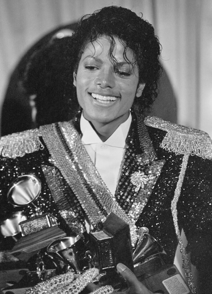 Alt = Superstar Michael Jackson holds several Grammy Awards he won at the 1984 Grammy Award ceremonies at the Shrine Auditorium in Los Angeles Tuesday. His top award was the album of the year, "Thriller," which sold nearly 30 million copies. By United Press International ©Creative Commons Attribution
Michael Movie Billion-Dollar Success